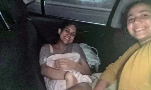 A mãe Patricia Praia segurando a filha no colo, ao lado da doula Bruna Lima