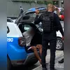 O preso (casaco branco) é levado para a Cidade da Polícia