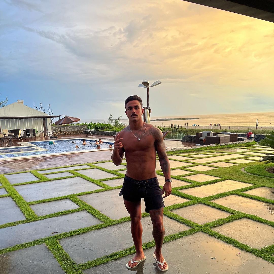 Anitta parace ajoelhada com um shortinho e um top com a logo da 'Furacaão 2000'. Já o rapaz está sem camisa, de bermuda azul e chinelos.