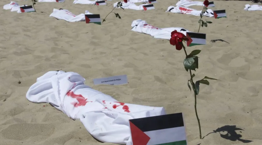 Panos brancos com manchas vermelhas, foram espalhados pela areia da praia, simbolizando corpos infantis