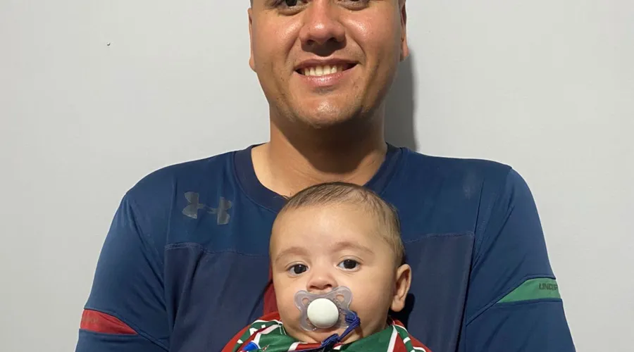 Gabriel segura o filho João Gabriel, de apenas quatro meses, que já herda o amor pelo Fluminense