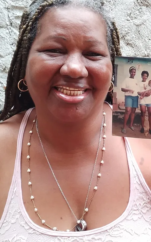 Renata segura um retrato. Na foto, ao lado de sua irmã e em seu colo, está a primeira filha, entregue para adoção com três meses de vida