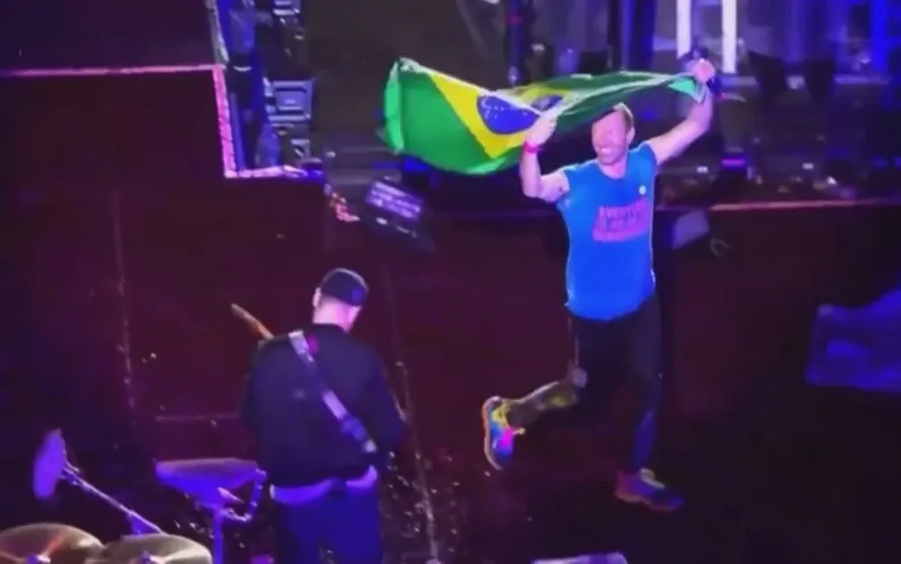 Chris Martin com a bandeira do Brasil joga por Bruno no palco