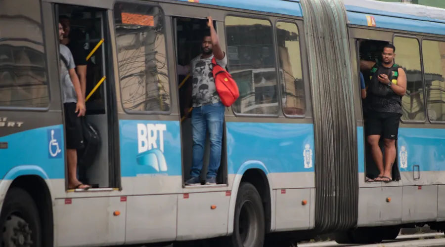 Passageiros em pé na porta de um ônibus do BRT: descaso