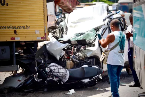 Carro e uma moto ficaram espremidos entre os caminhões